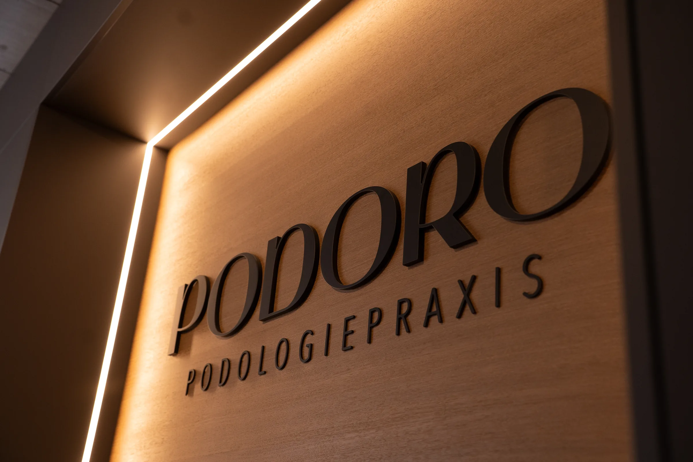 PODORO Podologiepraxis Muri AG – beleuchteter Praxisschriftzug im Empfangsbereich